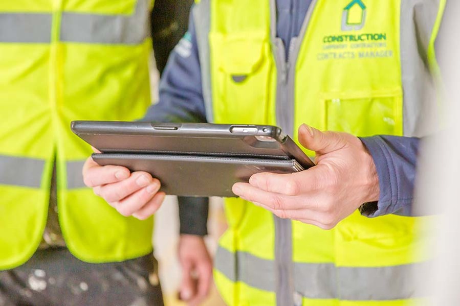 Construction workers in high-visibility jackets looking at tablet on site to improve health and safety measures
