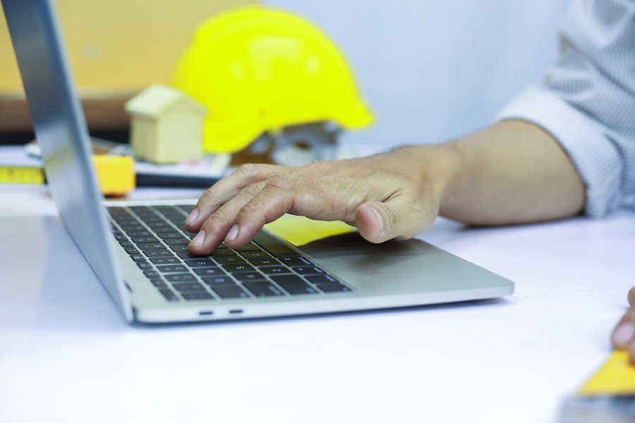 Contractor manager using a laptop in an office environment with a hardhat in the background
