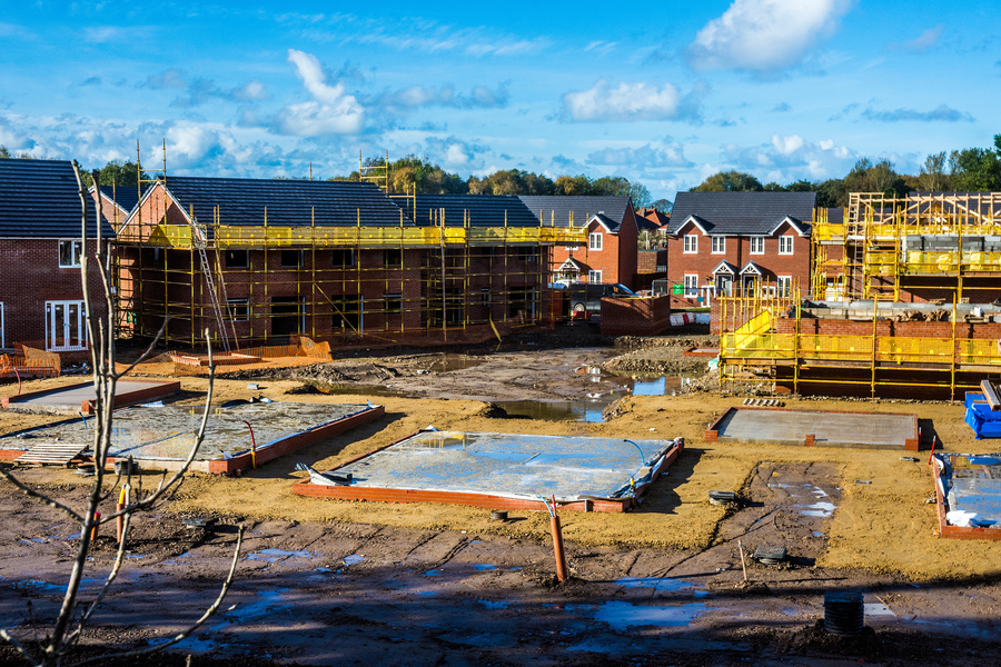 UK house building site with complete and partially complete new homes. Scaffolding surrounds incomplete houses and new plots are marked out in the early stages of new builds.